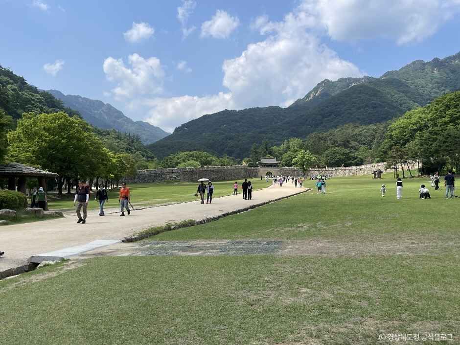 문경새재도립공원 초입 넓은 잔디밭과 성곽, 뒤로 이어지는 산 능선